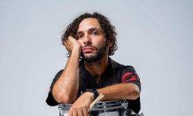 Orlando Muñiz with drum sticks, sitting on backward chair