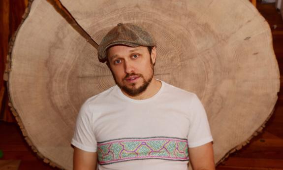 Ryan Montbleau poses while wearing a brown cap and white t-shirt. 