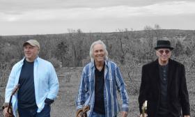 Trio of musicians, 2PM band, amiling, walking on hilltop with mountains in the background