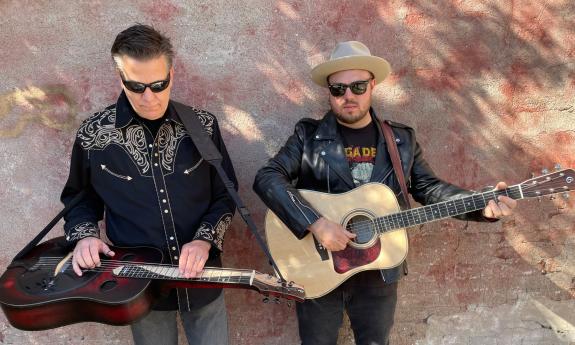 Rob Ickes on dobro, and Trey Hensley on guitar, standing against a painted wall