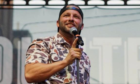 Dustin Sims smiles and holds a mic to his lips on stage. 