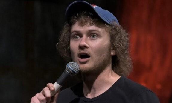 Casey Rocket speaks in front of a red and black backdrop. 