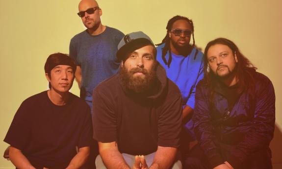 Bandmates from Pretty Lights smile and pose in front of a yellow backdrop. 