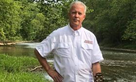 Mike stands in nature with a waterway and trees behind him