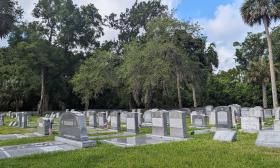 A view of a cemetery, with trees along the edge and inscriptions in Hebrew and English