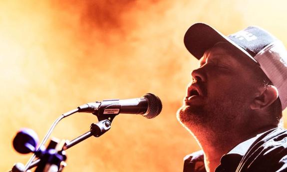 Songwriter Blue Foley singing with microphone, with orange background.