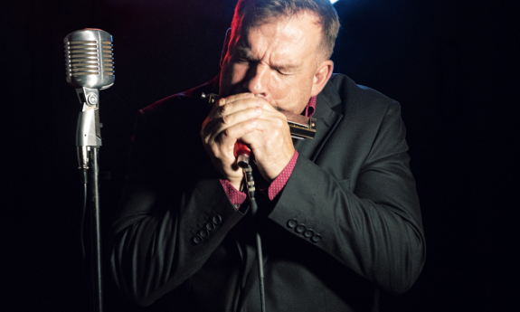 Chris O'Leary shuts his eyes while playing the harmonica on stage. 