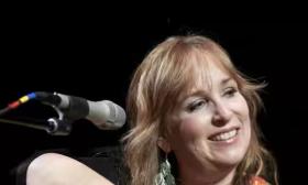 Songwriter Gretchen Peters smiling, in front of microphone, onstage