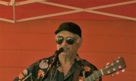 Musician Al Canali in sunglasses with guitar in front of a mic