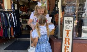 A staff-person at the Harley-Davidson shop on St. George Street hands out candy to a young lady costumed as "Dorothy" 