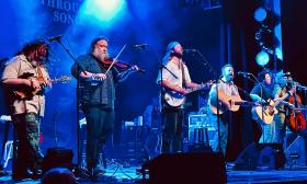 The six front members of Trampled by Turtles, on stage under a blue light