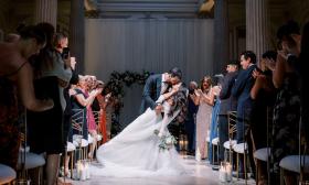 A groom holds his bride who is leaning back as they kiss in the aisle after the wedding