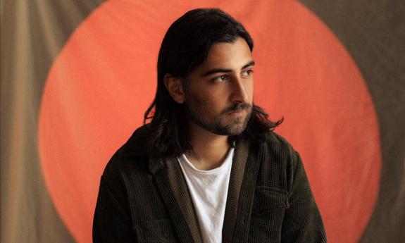 Artist Noah Kahan posing against a minimalist backdrop, framed by a red circle spotlight