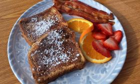 A plate of French toast, bacon, and fruit