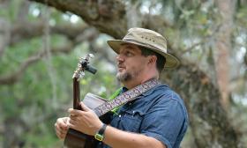 Musician, Michael Lagassee in a hat outside playing guitar