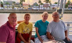 Two couples seated at a table on a boat with the bayfront in the background