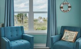 A hotel room with beach decor, two comfortable chairs, and a view of the dunes