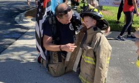 A firefighter kneeling beside a young boy dressed in fire gear