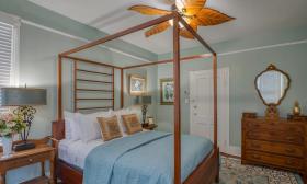 A tall wooden frame over the bed makes a statement in this light blue room with polished wood furniture