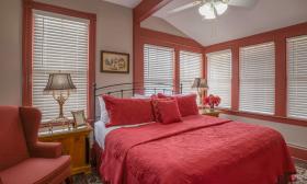 Taupe walls, painted molding, and a cheerful red bedspread greet guests in Juli, a room at Victorian House Bed and Breakfast