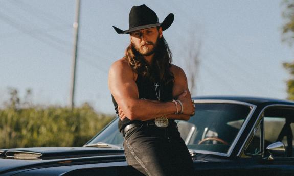 Warren Zeiders leans against a classic car, wearing a black cowboy hat.