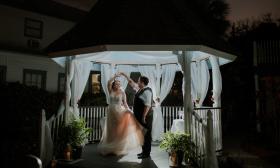 A bridal couple dance at night, on a softly-lit and draped gazebo 