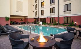 The pool deck has seating, lounge chairs, and fire-pit tables