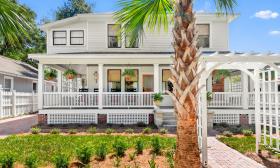 A two-story white home with arched entrance and a wrap-around porch