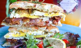 A tall breakfast sandwich, served with leafy greens on a blue plate