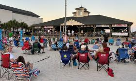 People lounging on the sand enjoying live music