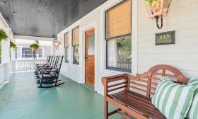 A settee and rocking chairs wait for guests on this front porch with a green floor