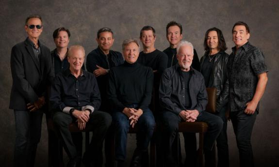 Bandmates from Chicago wear black and pose in front of a dark brown backdrop.