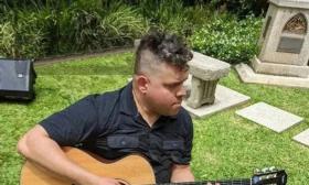 Edwin Barbosa outside playing guitar, in black shirt