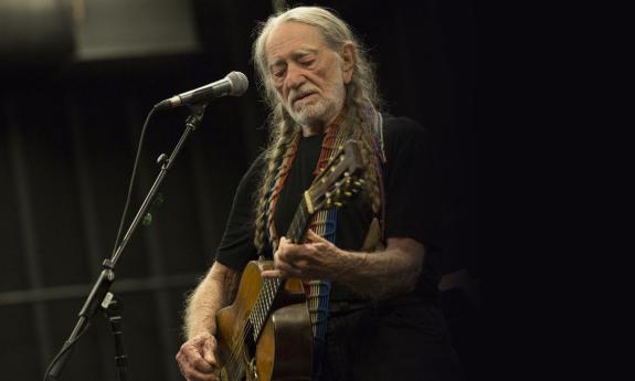 Willie Nelson performs on stage with his guitar.