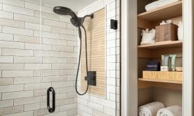 A modern shower with off-white stone tiles and a hand-held showerhead