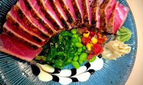 Slices of ahi tuna, with edaname and sauces, on a blue plate