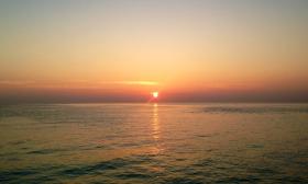 A sun set at sea shows a bright orange and deep red sky reflected in the water