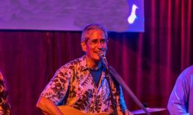 Al Johnson playing guitar and singing, on stage