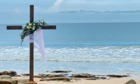 A cross on the beach, decorated for a beach wedding with roses and greenery and a white veil