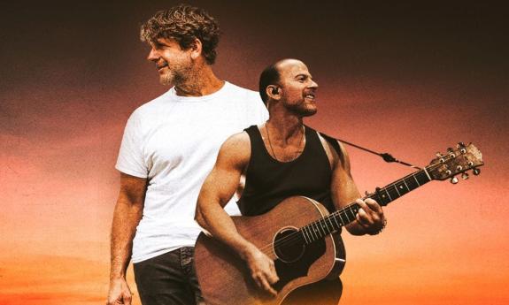 Billy Currington and Kip Moore smile and pose in front of a black and brown backdrop.