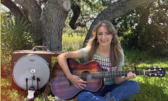 Brittani Meuller, 1 Woman Band with her multi-instruments, under a tree.