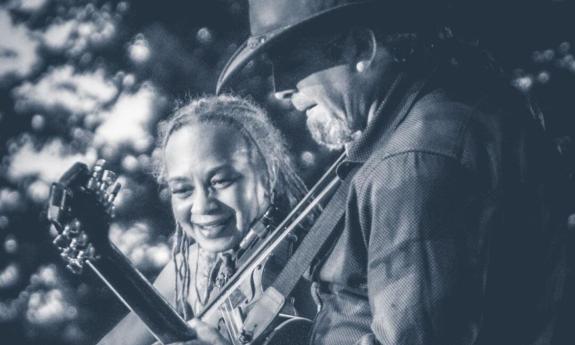 In a black and white photo, bandmates from the Gypsy Blue Revue share smiles as they play the guitar.