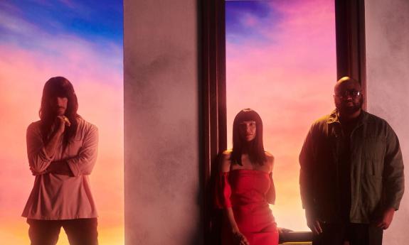 Bandmates from Khruangbin pose in front of a multicolored backdrop. 