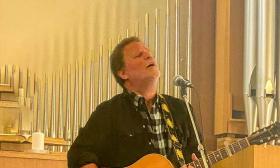 Musician Marc Douglas Berardo, singing, with pipe organ in the background