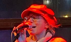 Musician She Fay, wearing a slouch hat, singing into a microphone