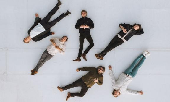 Bandmates from Wilco lay on a gray floor and pose for fans.