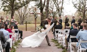 A military groom sweeps his bride into a kiss as the at an outdoor wedding with attendants and guests watching