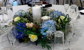 A blue table ring with small yellow roses and greenery centered around two candles on a guest table