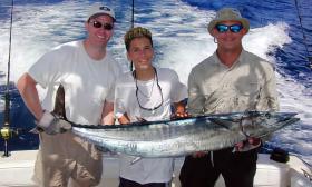 Three men carry a wahoo fish