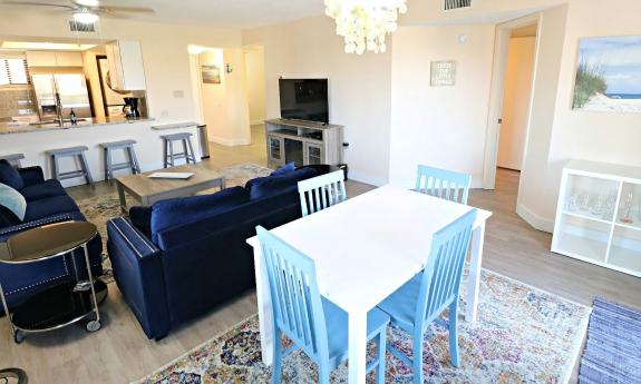 A dining table in the foreground, with living area and kitchen beyond on a sunny day